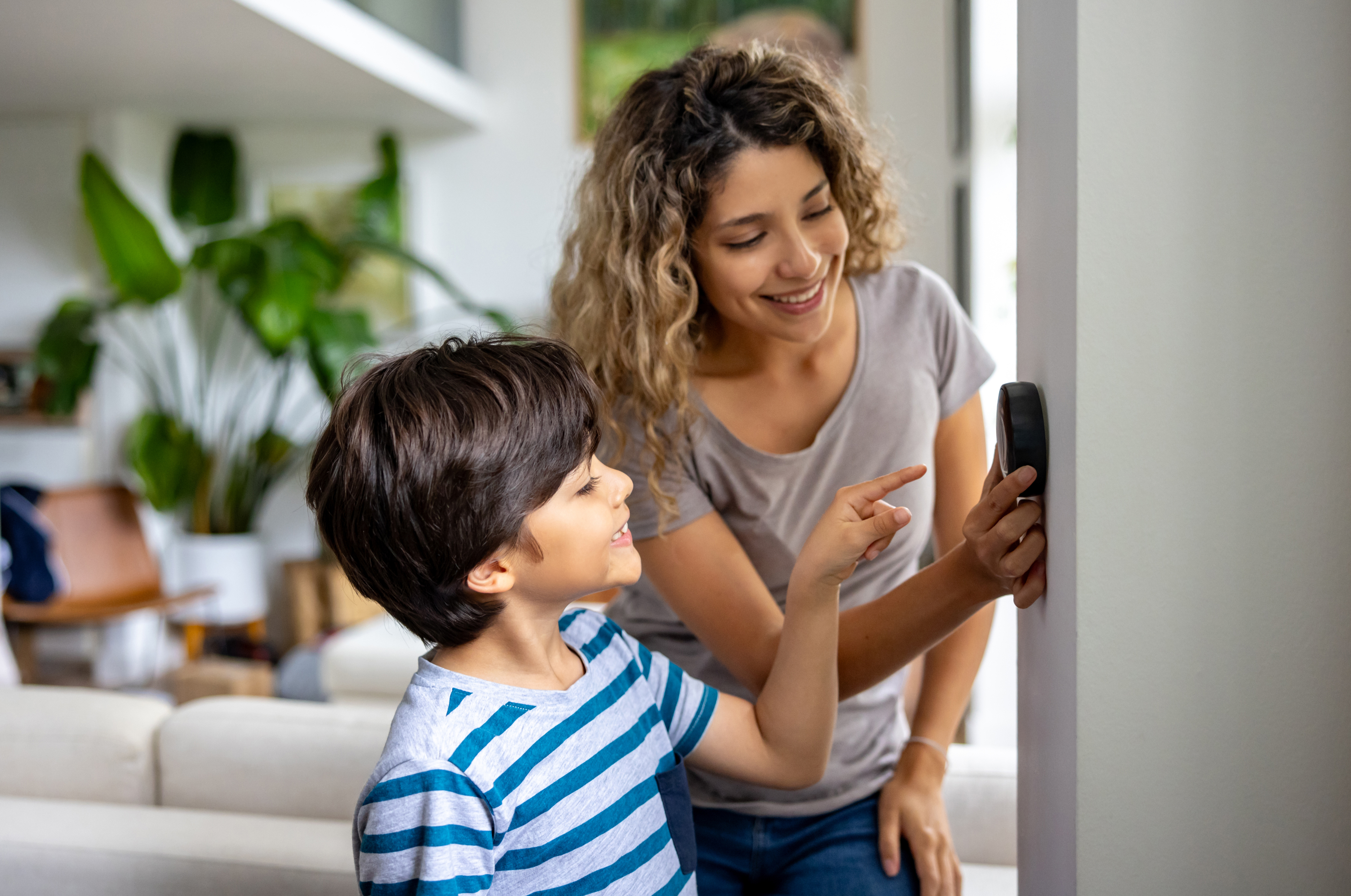 Happy mother and son at home using a smart thermostat to adjust the temperature - smart home concepts