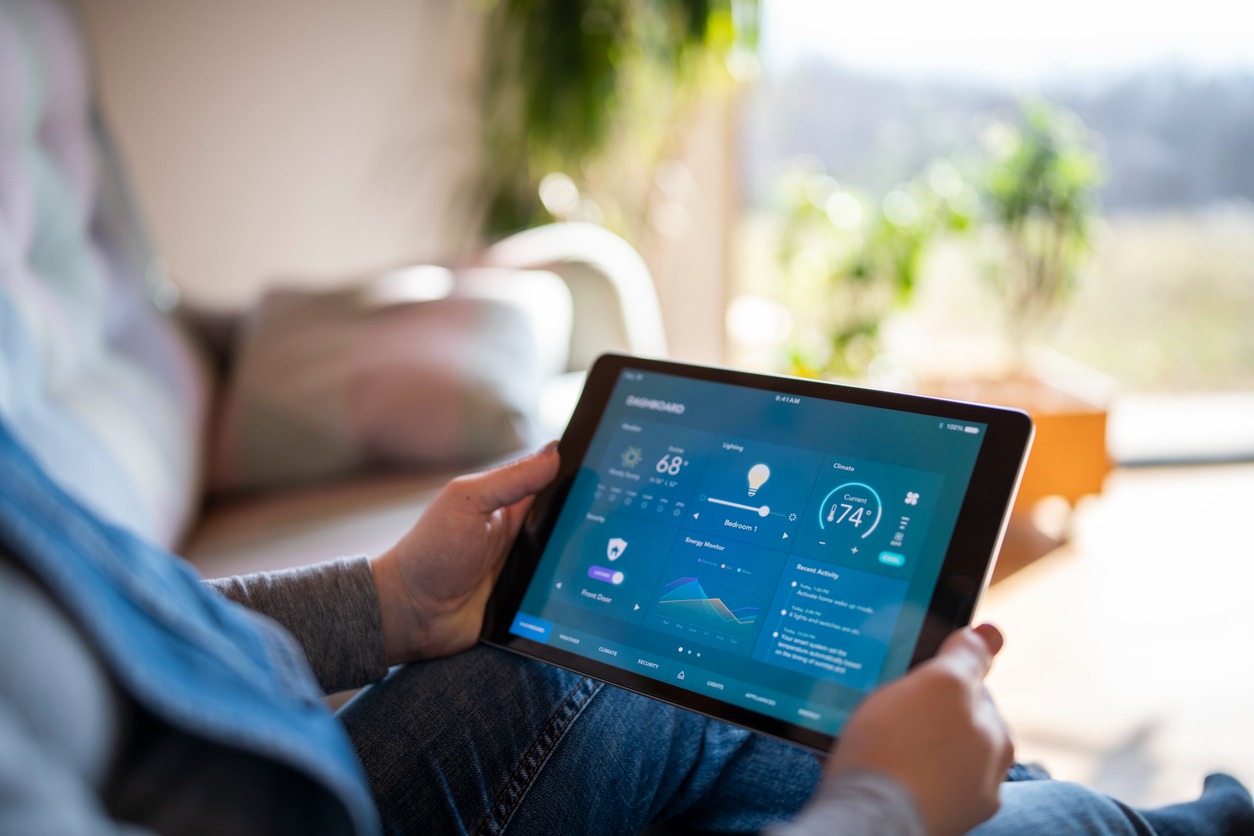 A person using a tablet to control home automation features, including lighting, climate, and energy monitoring, with a clear view of the dashboard interface.